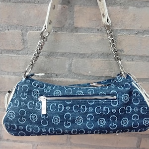 May include: A denim shoulder bag featuring a floral pattern and the letters "CD" repeated. It has a silver chain strap and a white leather handle. A silver zip is across the top. The bag is approximately 30 cm long.