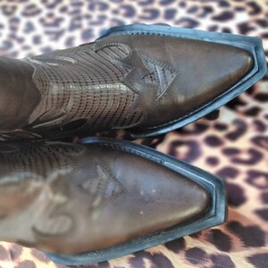 May include: A pair of brown leather cowboy boots with intricate stitching and a pointed toe. The boots are on a leopard print background.