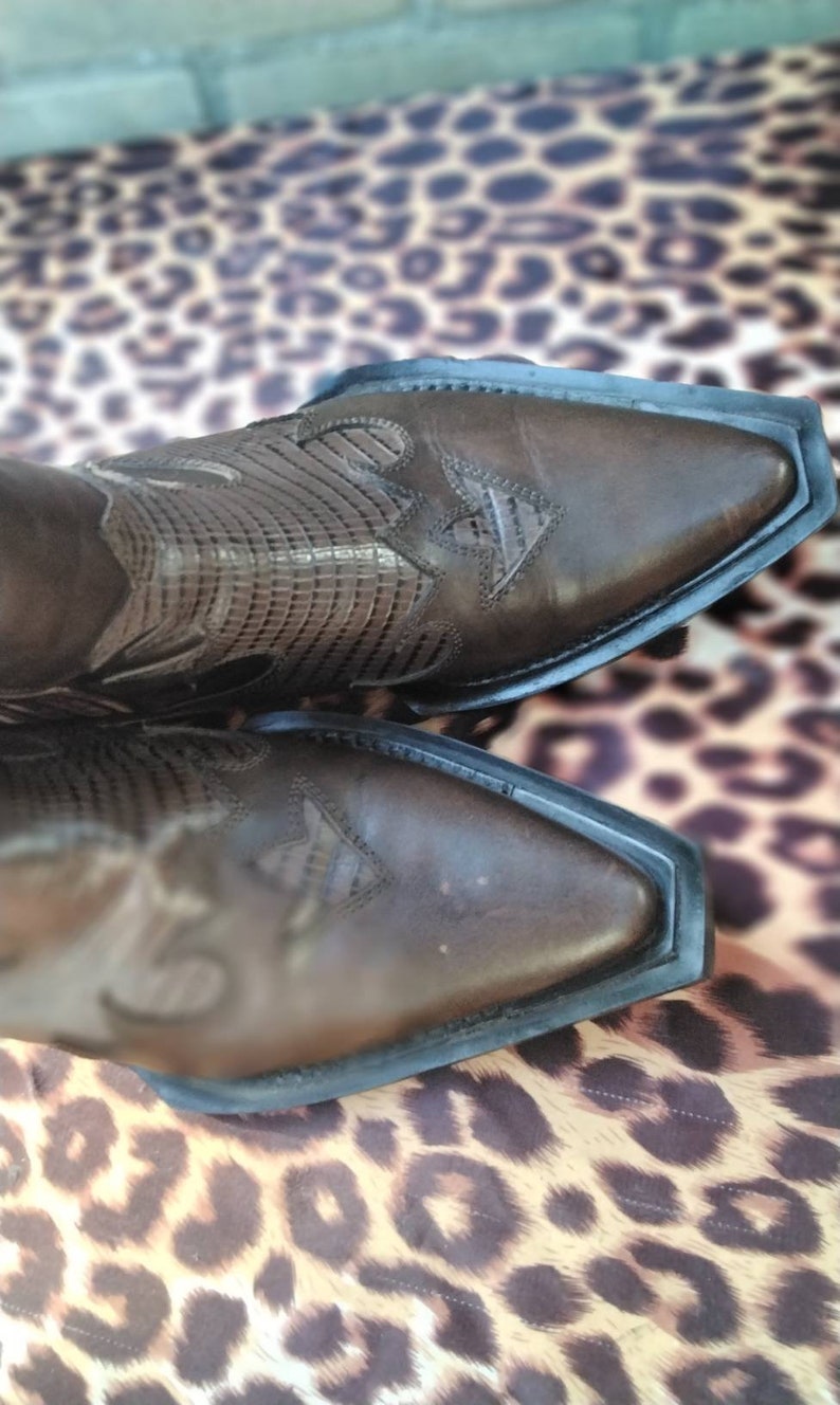 May include: A pair of brown leather cowboy boots with intricate stitching and a pointed toe. The boots are on a leopard print background.