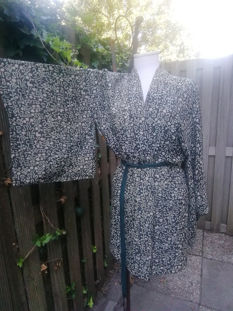 May include: A black and white patterned kimono robe with a green sash. The robe has a V-neck and long sleeves.