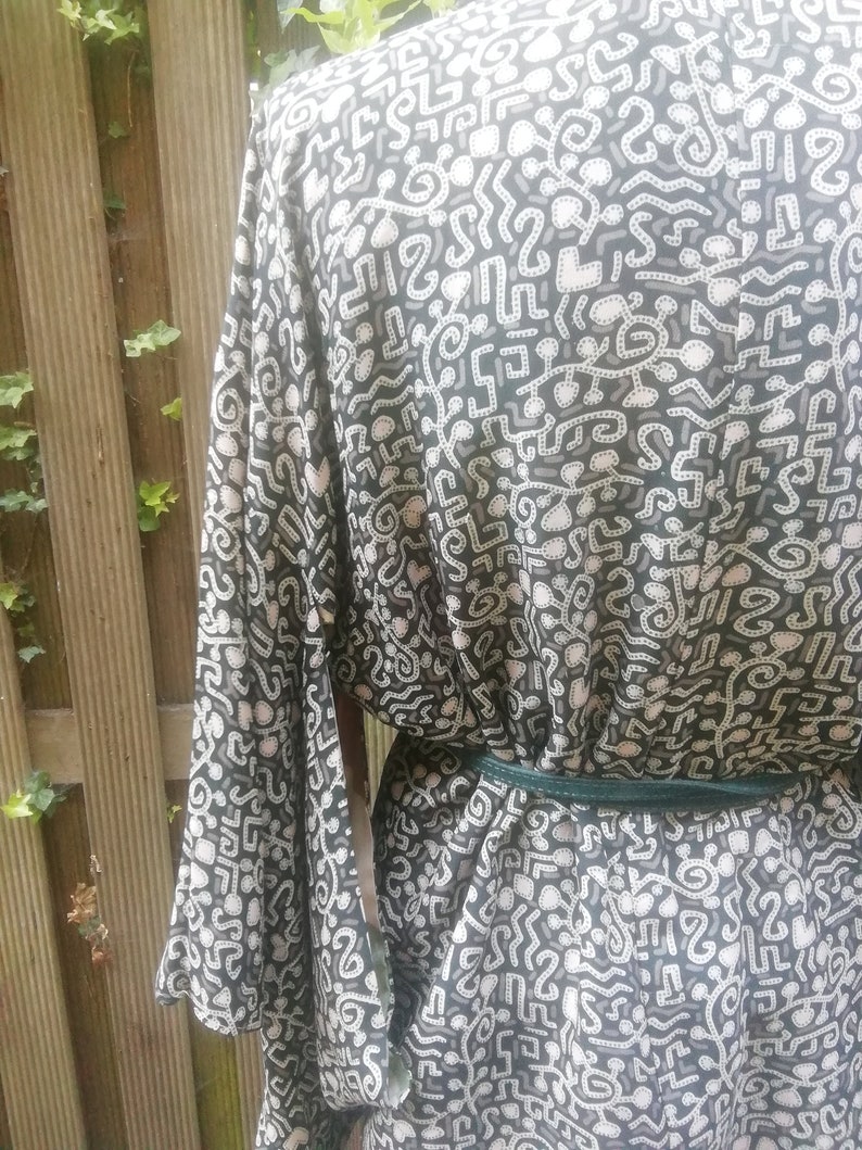 May include: A black and white patterned kimono with a green sash. The pattern is made up of abstract shapes and lines.