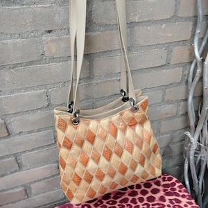 Op de afbeelding: Een beige leren handtas met een ruitvormig patroon. De tas heeft twee hengsels en een ritssluiting bovenaan.