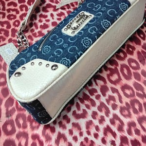 May include: A denim and white handbag with a silver chain strap. The bag has a blue denim top with a floral pattern and a white textured base. Silver studs and a silver logo plate add detail.