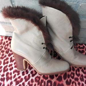 May include: A pair of light brown leather ankle boots with fur trim around the top. The boots have a chunky heel and lace-up closure.