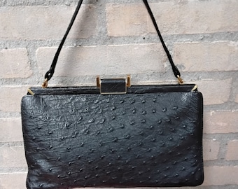 May include: A black ostrich leather handbag with a gold clasp and a single strap.