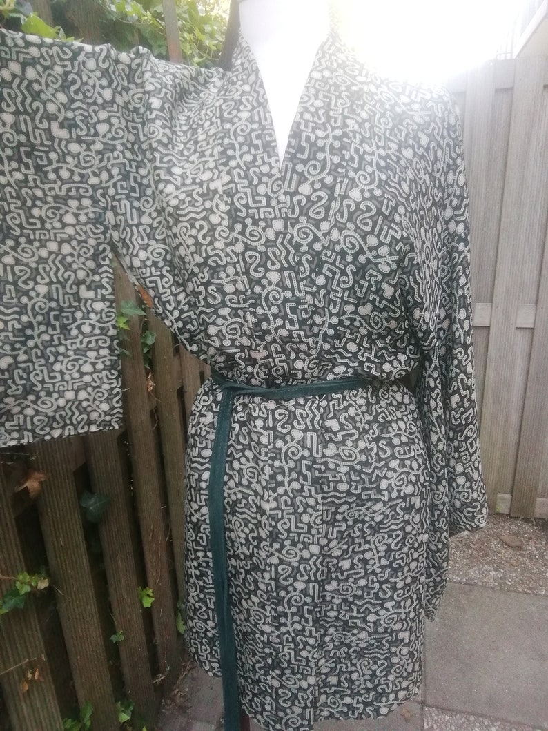 May include: A black and white patterned kimono robe with a green sash. The pattern is made up of abstract shapes and lines.