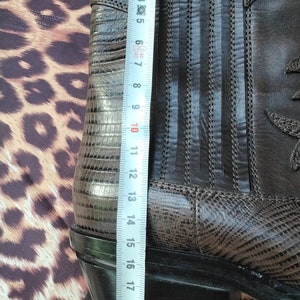 May include: Brown leather cowboy boots with a snakeskin pattern on the side and a black rubber sole. The boots are measured with a tape measure, showing a length of 22 inches.