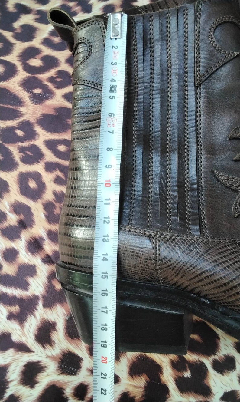May include: Brown leather cowboy boots with a snakeskin pattern on the side and a black rubber sole. The boots are measured with a tape measure, showing a length of 22 inches.