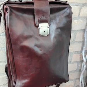 May include: A dark brown leather briefcase with a silver lock and a shoulder strap. The bag has a flap closure and a top handle.