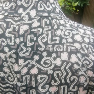 May include: Black fabric with a white and pink abstract pattern. The pattern features a variety of shapes and lines, including circles, squares, and squiggles.