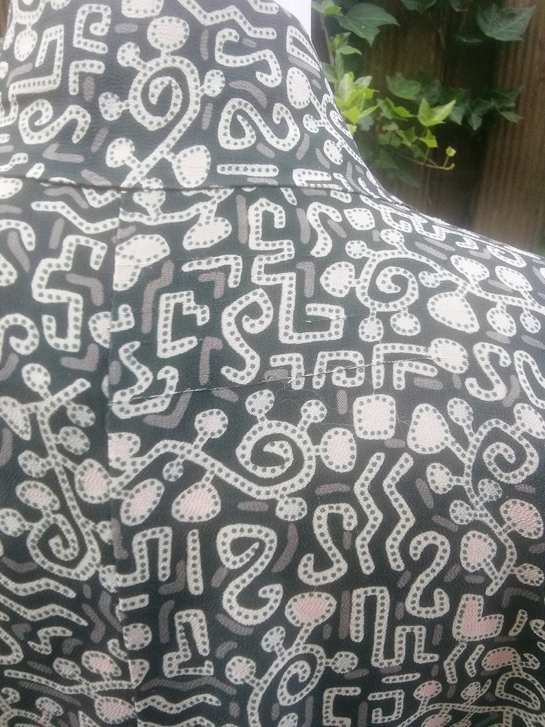 May include: Black fabric with a white and pink abstract pattern. The pattern features a variety of shapes and lines, including circles, squares, and squiggles.