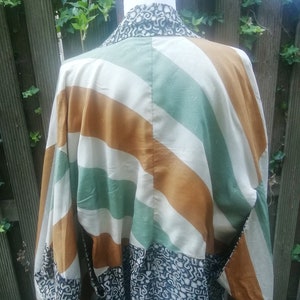May include: A white, green, and brown striped kimono with a black and white patterned fabric on the bottom. The kimono has long sleeves and a wide collar.
