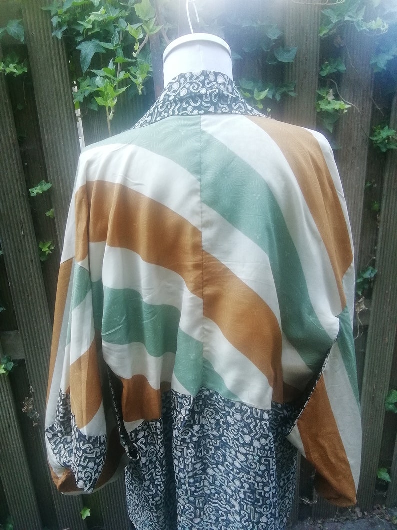 May include: A white, green, and brown striped kimono with a black and white patterned fabric on the bottom. The kimono has long sleeves and a wide collar.