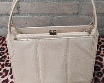 May include: A vintage beige handbag with a snakeskin pattern. The bag has a rectangular shape with a clasp closure and two rounded handles. The bag is made of a textured material and has a classic, elegant design.