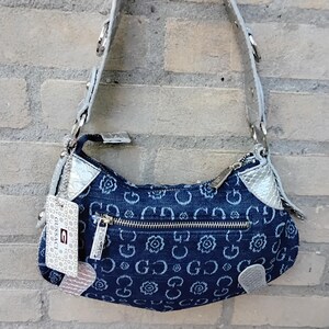 May include: A denim shoulder bag with a silver strap and accents. The bag features a repeating pattern of white floral and "G" designs. A silver zip and a tag with the brand name are visible.
