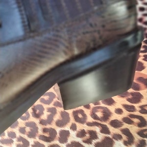 May include: A brown leather boot with a black rubber sole. The boot is sitting on a leopard print fabric.