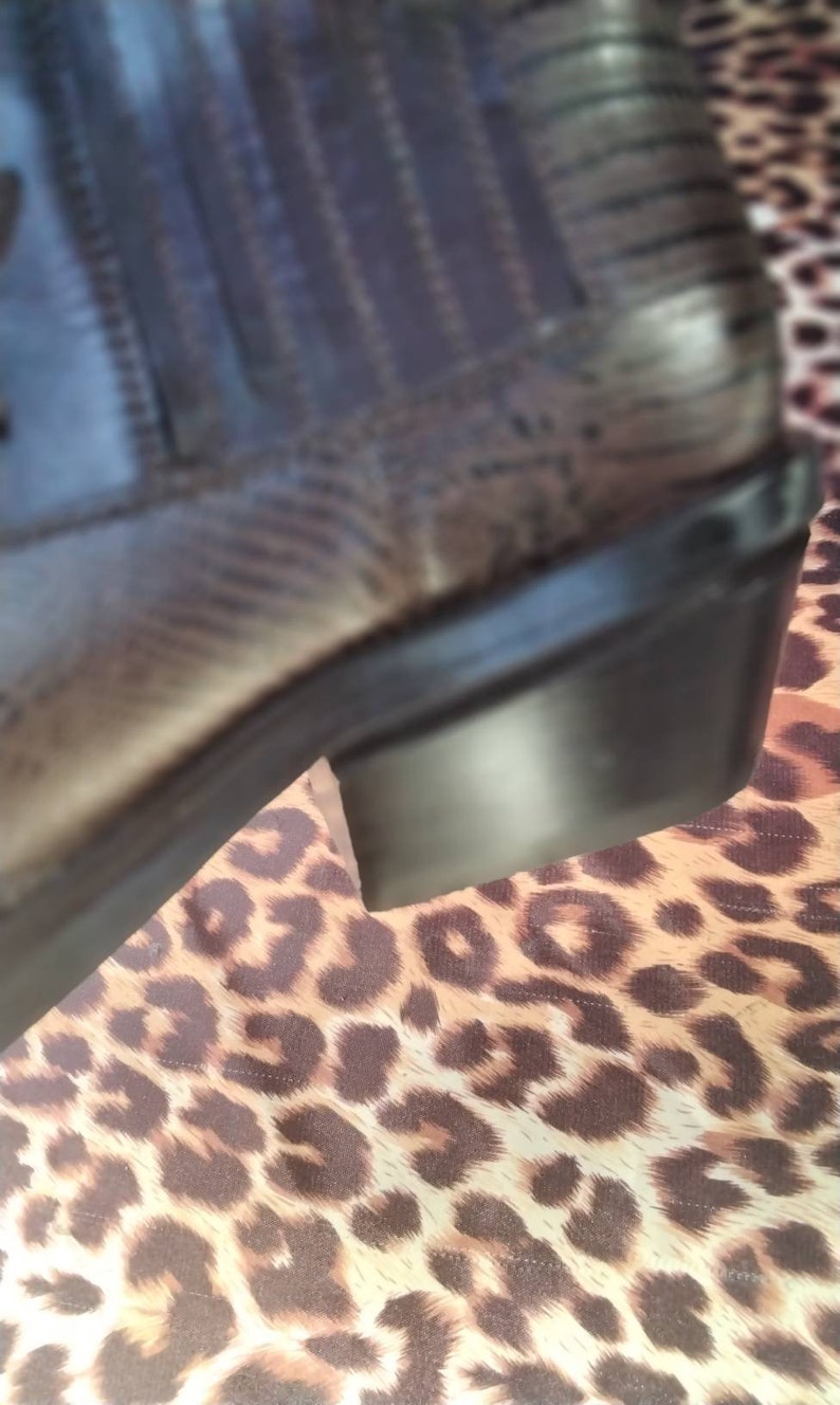May include: A brown leather boot with a black rubber sole. The boot is sitting on a leopard print fabric.