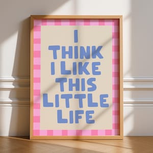 May include: Wooden framed art print with the text "I THINK I LIKE THIS LITTLE LIFE" in blue letters on a beige background. The print has a pink and white checkered border.