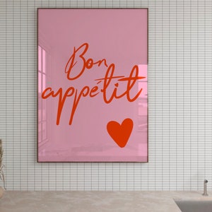 Puede incluir: Un p&oacute;ster enmarcado en rosa con el texto "Bon app&eacute;tit" en escritura cursiva roja. Un coraz&oacute;n rojo se encuentra en la esquina inferior derecha del p&oacute;ster.