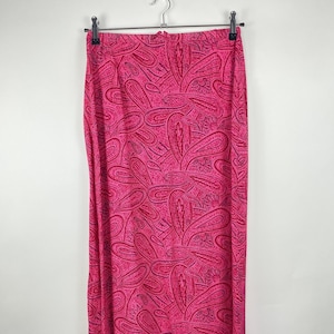 Peut inclure: Longue jupe rose vif avec un motif cachemire. La jupe est suspendue à un cintre en métal sur un fond blanc. Le motif cachemire présente une couleur rose plus foncée à l'intérieur des grandes formes roses.