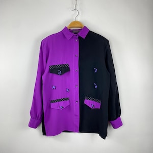 Könnte beinhalten: Ein zweifarbiges Hemd mit Knöpfen, vertikal geteilt mit einem lila und schwarzen Design. Die lila Seite hat zwei Taschen mit schwarzem Tupfenbesatz und lila gestickten Details. Die schwarze Seite hat passende gestickte Details. Lange Ärmel mit lila Manschetten.