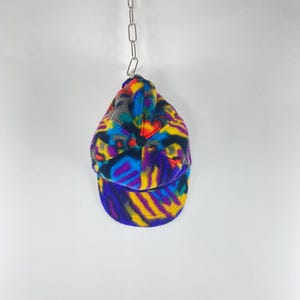 Peut inclure: Casquette de baseball à motif avec une visière incurvée, suspendue à une chaîne argentée. Le motif de la casquette présente un mélange de couleurs vives, notamment le bleu, le jaune, le violet et l'orange. Le motif du chapeau crée un motif unique et accrocheur.