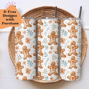 May include: Three stainless steel tumblers with a white background and a repeating pattern of gingerbread men with brown icing and red buttons. The gingerbread men are surrounded by green leaves and light brown flowers.
