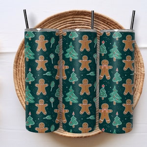 May include: Three stainless steel tumblers with a green background and a repeating pattern of gingerbread men and Christmas trees. The tumblers are sitting on a woven basket.