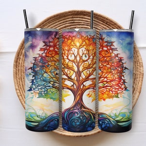 May include: Three stainless steel tumblers with a colorful watercolor tree of life design. The artwork features a vibrant spectrum of colors, including blues, oranges, and greens. Each tumbler has a black straw and a silver lid. The tumblers are displayed on a woven tray.