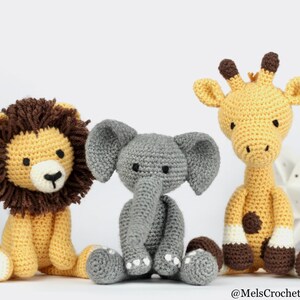 May include: Three crocheted stuffed animals: a yellow giraffe, a gray elephant, and a yellow lion with a brown mane. The animals are sitting on a white surface.