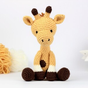 May include: A crocheted giraffe toy with brown ears, brown spots, and brown hooves. The giraffe is sitting with its legs crossed.