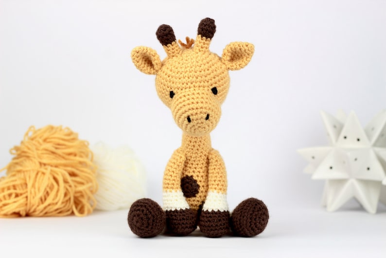 May include: A crocheted giraffe toy with brown ears, brown spots, and brown hooves. The giraffe is sitting with its legs crossed.