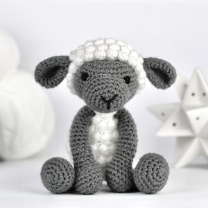 May include: A gray and white crocheted sheep toy with a fluffy white fleece. The sheep has a small black nose and black eyes.