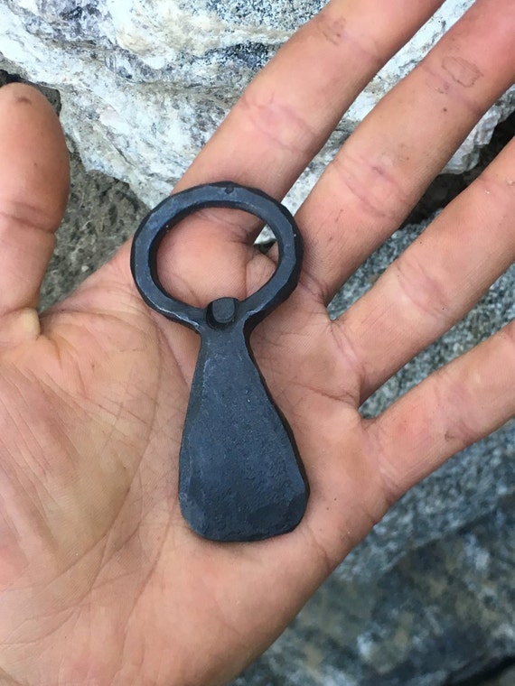 Hand-forged at an actual anvil — the hammer marks and raw iron texture make this a bottle opener that looks like it belongs in a blacksmith's portfolio, not a gift shop.