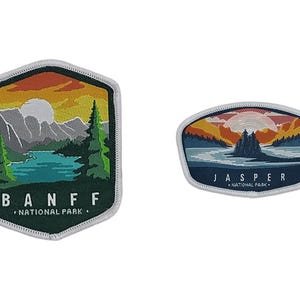 Op de afbeelding: Twee geborduurde patches met berglandschappen. De linker zeshoekige patch toont Banff National Park met een meer, bomen en bergen. De rechter ovale patch toont Jasper National Park met een meer, bomen en een lucht bij zonsondergang.
