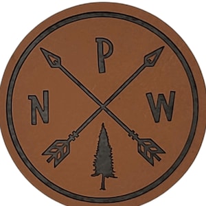 May include: A brown leather coaster with a black design. The design features a compass with arrows pointing north, west, and a pine tree in the center. The letters "P", "N", and "W" are also included in the design.
