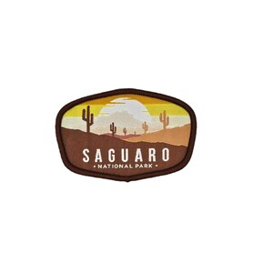 May include: A brown embroidered patch with a sunset scene of saguaro cacti in the desert. The text "SAGUARO NATIONAL PARK" is printed in white below the scene.