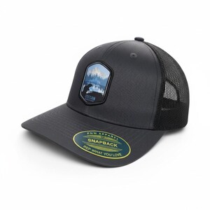 Könnte beinhalten: Eine anthrazitfarbene Snapback-Kappe mit schwarzem Mesh-Rücken. Auf der Vorderseite befindet sich ein Aufnäher mit einer Berg- und Bärenszene und dem Wort "OREGON". Die Kappe hat außerdem einen gebogenen Schirm und ein Etikett mit der Aufschrift "PNW APPAREL SNAPBACK REP WHAT YOU LOVE."