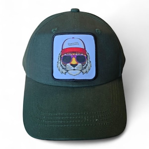 May include: A green baseball cap with a patch featuring a cartoon tiger wearing sunglasses and a red and white trucker hat. The patch says "Trucker" on the hat.