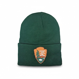 Pode incluir: Um gorro de malha verde escuro com uma aba dobrada. O gorro apresenta um patch com as palavras "National Park Service" e um gráfico de uma montanha, árvores e um bisonte.