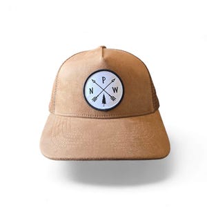 May include: A brown suede and mesh trucker hat with a white patch featuring a compass design and the text "N W P" and a pine tree.