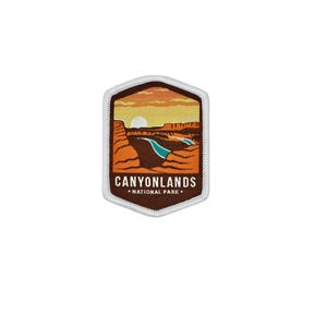 Puede incluir: Un parche del Parque Nacional de Canyonlands que presenta una escena de paisaje con una puesta de sol, un cañón y un río. El parche tiene un borde blanco y el texto "CANYONLANDS NATIONAL PARK" en naranja y blanco.