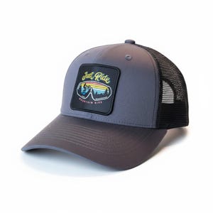 Può includere: Cappellino da camionista grigio con retro in rete nera e visiera curva. La parte anteriore presenta una toppa quadrata nera con la scritta "Just Ride Mountain Bike" sopra una colorata scena di mountain bike.