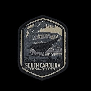 May include: A black and white embroidered patch with a silhouette of a bird in front of a tree. The patch has a beige border and the text "SOUTH CAROLINA THE PALMETTO STATE" in white.