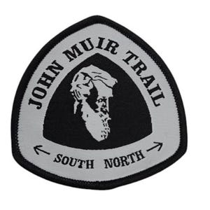 May include: A gray and black triangular patch with the text "John Muir Trail" in a white circle around a black silhouette of a mountain range. The text "South" and "North" are below the circle with arrows pointing in opposite directions.