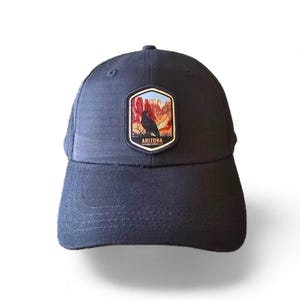 May include: A black baseball cap with a patch featuring a red rock formation and a black bird, with the text "ARIZONA" and "THE GRAND CANYON STATE" below the image.