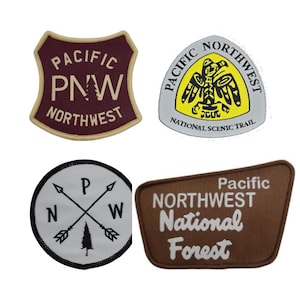 May include: Four embroidered patches featuring Pacific Northwest themes. One maroon shield-shaped patch reads Pacific PNW Northwest. One white circular patch shows crossed arrows and a tree. One yellow and white triangular patch reads Pacific Northwest National Scenic Trail. One brown trapezoidal patch reads Pacific Northwest National Forest.