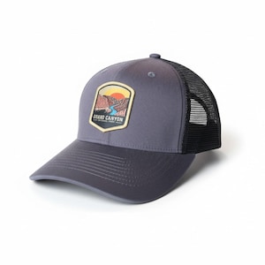 Puede incluir: Gorra de béisbol gris con la parte trasera de malla negra y visera curva. La gorra presenta un parche con un paisaje del Gran Cañón y el texto "GRAND CANYON NATIONAL PARK".