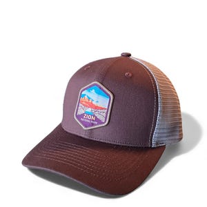 Puede incluir: Gorra de camionero marrón con parte trasera de malla y visera curva. La parte delantera presenta un parche con un diseño de paisaje y el texto "ZION NATIONAL PARK". La gorra es de color marrón oscuro con la parte trasera de malla blanca.