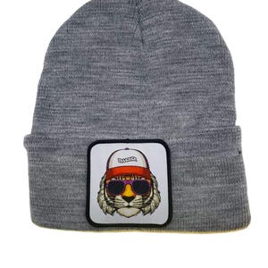 May include: Gray knitted beanie with a white patch featuring a tiger wearing sunglasses and a red baseball cap with the word "Trucker" on it.